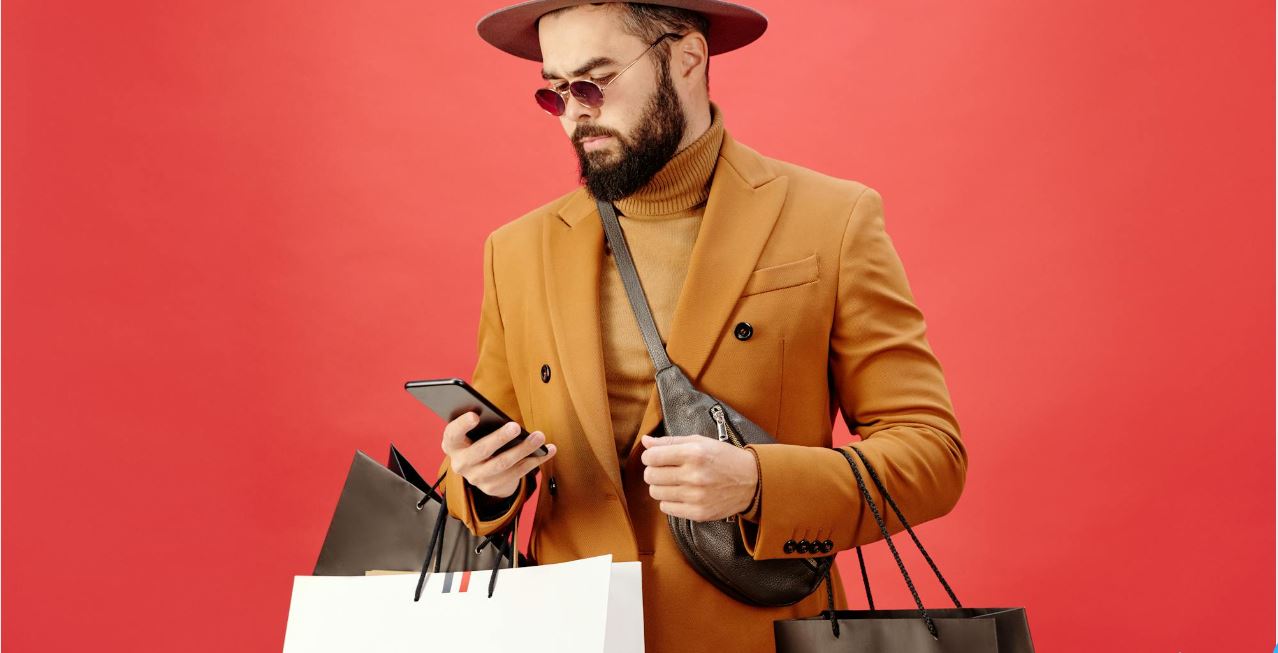 a man with sunglasses having alot of shopping bags and using mobile phone